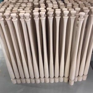 May include: A close-up view of a large group of unfinished wooden baseball bats standing upright. The bats are all the same size and shape, and they are arranged in a neat row.