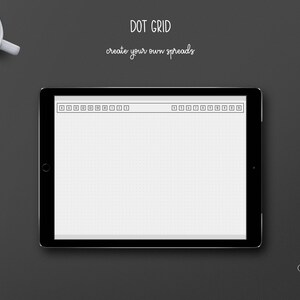 May include: A digital tablet displaying a dot grid layout with the text "DOT GRID create your own spreads." A white coffee cup and two silver paper clips are on a dark gray surface.