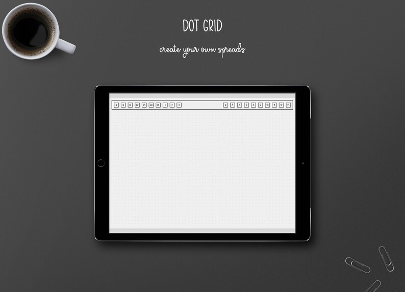 May include: A digital tablet displaying a dot grid layout with the text "DOT GRID create your own spreads." A white coffee cup and two silver paper clips are on a dark gray surface.
