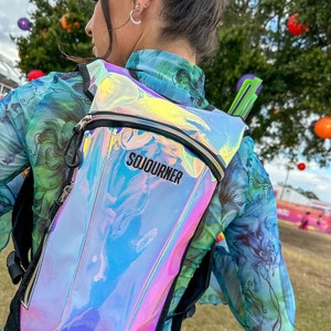 May include: A holographic iridescent backpack with a black zipper and the word "SOJOURNER" printed in black on the front.