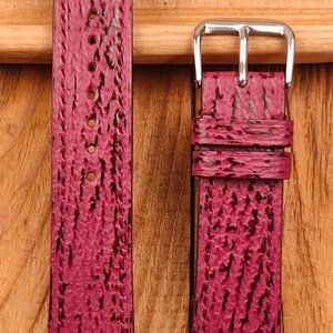 May include: Two-piece watch strap in a deep burgundy color with a textured, patterned surface. The strap has a silver-colored buckle and several holes for adjustment. The material appears to be leather or a leather-like material.