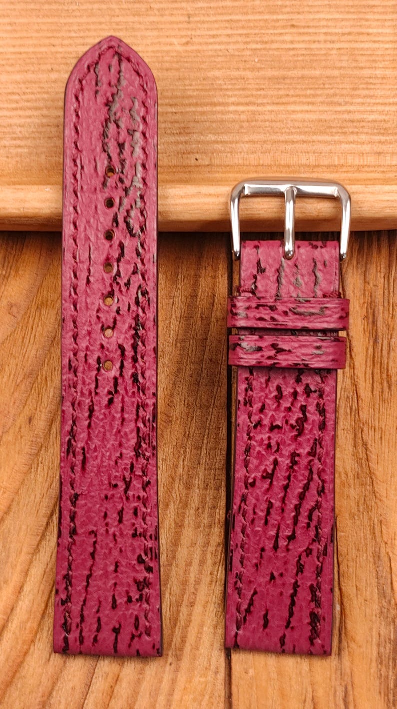 May include: Two-piece watch strap in a deep burgundy color with a textured, patterned surface. The strap has a silver-colored buckle and several holes for adjustment. The material appears to be leather or a leather-like material.