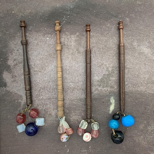 May include: Four wooden knitting needles with colorful glass beads attached to the bottom. The beads are in shades of blue, red, and white.