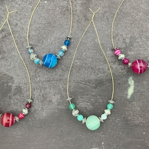 Puede incluir: Tres collares con cuentas de ágata. Los collares están hechos con cuentas plateadas y presentan una gran cuenta de ágata azul, verde y rosa.