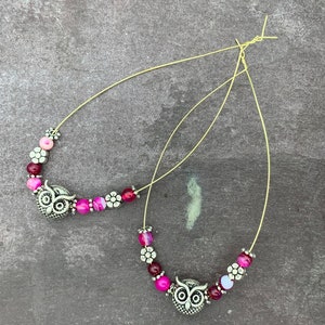 May include: A pair of silver owl charm earrings with pink and white beads on a gold wire.