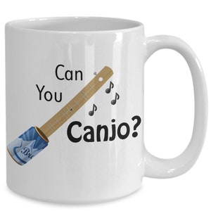 May include: White ceramic coffee mug with a black and white illustration of a canjo, a musical instrument made from a can and a stick. The text "Can You Canjo?" is printed on the mug.