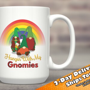 May include: White ceramic coffee mug featuring a rainbow and three gnomes holding a beer mug. The text "Hangin' With My Gnomies" is printed on the mug.