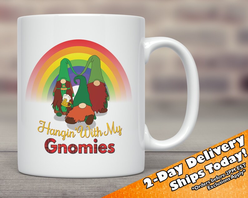 May include: White ceramic mug featuring a rainbow and three gnomes holding a beer. The text "Hangin' With My Gnomies" is printed on the mug in a red and black tartan font.