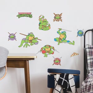 May include: Wall decals featuring Teenage Mutant Ninja Turtles characters in action poses. The set includes the Turtles with their signature weapons, logos, and a pizza slice. The decals are in green, blue, red, and purple.