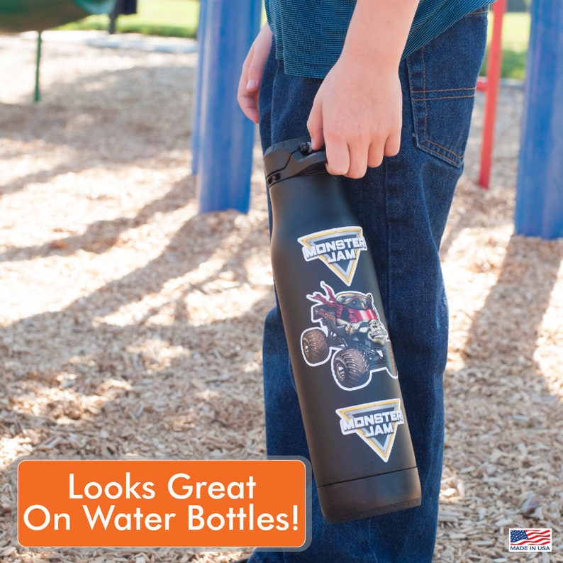 May include: A black water bottle with two Monster Jam stickers. The stickers feature a monster truck and the Monster Jam logo. The bottle is being held by a person wearing blue jeans.