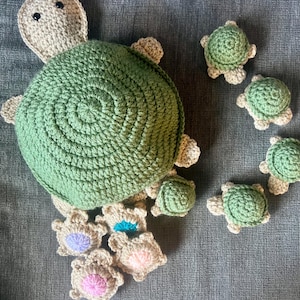 May include: A large green crocheted turtle with smaller crocheted turtles attached to its shell. The smaller turtles have different colored centers.