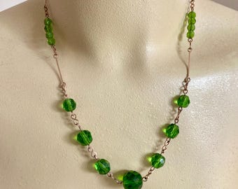 Peut inclure: Un collier de perles vertes avec une chaîne de couleur cuivre. Le collier présente des perles vertes à facettes de différentes tailles, enfilées le long d'une chaîne délicate. Le collier est présenté sur un mannequin.
