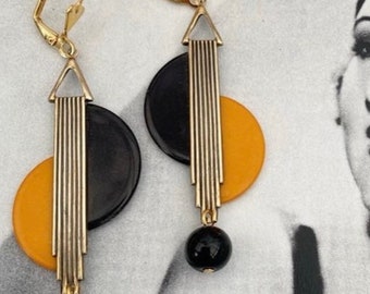 May include: A pair of gold tone earrings with black and yellow geometric shapes and black beads. The earrings have a modern art deco style.