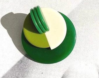 May include: A green and white geometric brooch with a layered design. The brooch is made of plastic and has a circular shape.