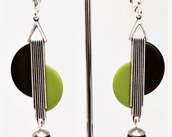 May include: A pair of silver tone clip-on earrings with black and green geometric shapes. The earrings feature a black half-circle, a green half-circle, and a silver vertical bar with lines. The earrings are finished with a black bead.