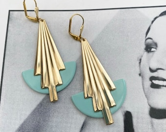 May include: A pair of gold-tone earrings with a geometric design. The earrings feature a fan-shaped design with a half-circle of light blue plastic at the bottom.