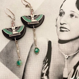 May include: Silver leverback earrings. Each earring features a black, semi-circular design with a silver and enamel figure. A dangling silver bar and a faceted, teal bead complete the design. The earrings are approximately 6 cm long.