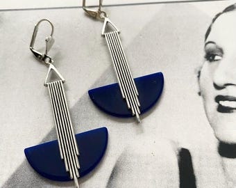 May include: A pair of Art Deco earrings. Each earring has a silver-toned, vertical design with parallel lines above a semi-circular, deep blue element. The earrings have a lever-back closure.