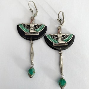 May include: A pair of silver earrings with a leverback clasp. Each earring has a black, semi-circular base with a silver figure and green and black wing design. A silver bar and a green bead hang from each earring.