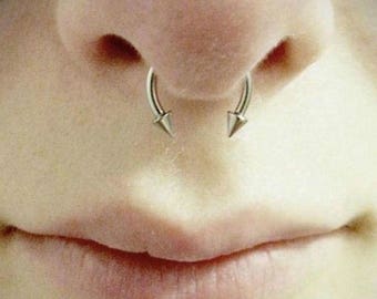 May include: Close-up of a person's nose with two silver septum rings with pointed ends.