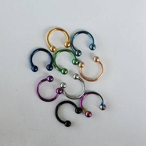 May include: A set of eight colorful horseshoe-shaped rings with ball ends. The rings are made of metal and come in a variety of colors, including gold, silver, blue, green, purple, and black.