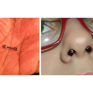 May include: A close-up of a person's nose with a small silver nose ring. The person is wearing red-framed glasses.