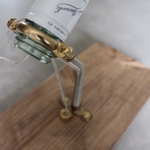 May include: A repurposed Bacardi rum bottle with a custom brass spout and a wooden base. The bottle's label is visible, and the spout is attached with a wire. The wooden base is a light brown color.