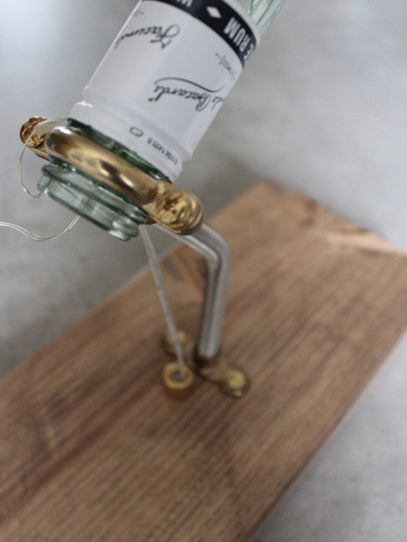 May include: A repurposed Bacardi rum bottle with a custom brass spout and a wooden base. The bottle's label is visible, and the spout is attached with a wire. The wooden base is a light brown color.