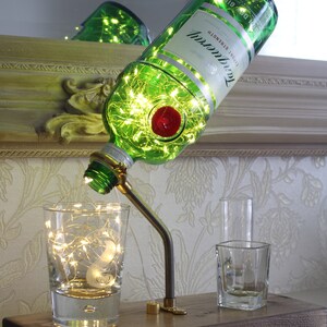 May include: A repurposed green glass bottle lamp with internal fairy lights, a red wax seal, and the Tanqueray logo. The lamp is mounted on a wooden base with a flexible metal arm, illuminating a glass and two shot glasses.