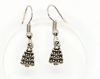 May include: A pair of silver-colored Christmas tree earrings. Each earring features a detailed tree charm with small, round accents. The earrings have a hook closure and are displayed on a clear, circular surface against a white background.