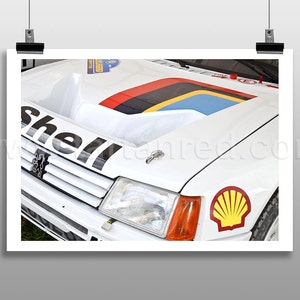 Peut inclure: Gros plan d'une voiture de course Peugeot blanche vintage. Le capot présente un motif de rayures multicolores et le mot "Shell" en grandes lettres noires. Un logo Shell est visible sur le côté.
