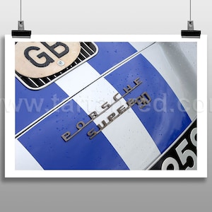 May include: A close-up of a silver Porsche Super 90 race car with a blue and white racing stripe. The car has a GB license plate and water droplets on the bonnet.