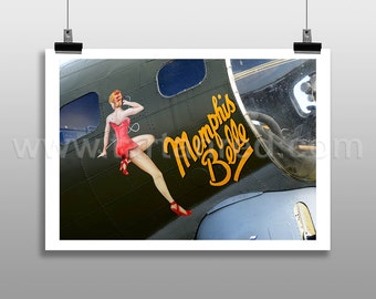 May include: A green and gray World War II era bomber plane with the words "Memphis Belle" painted in yellow on the side. A pin-up girl in a red dress is painted on the side of the plane.