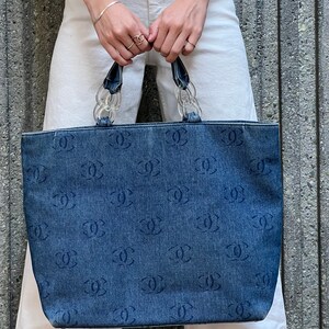 May include: A blue denim tote bag with a clear plastic chain handle and a repeating pattern of the letter "C".