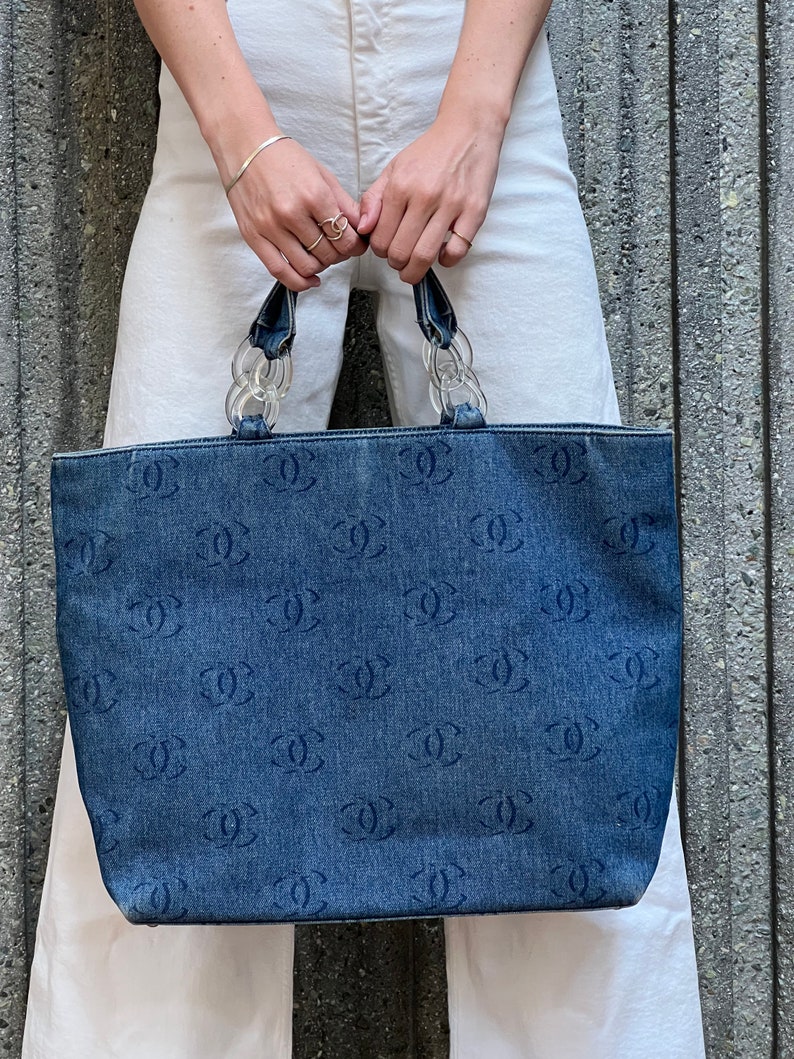 May include: A blue denim tote bag with a clear plastic chain handle and a repeating pattern of the letter "C".