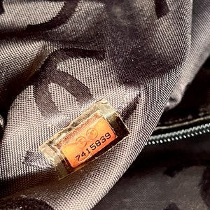 May include: Close-up of a black fabric bag with a brown leather tag that reads "7415839".