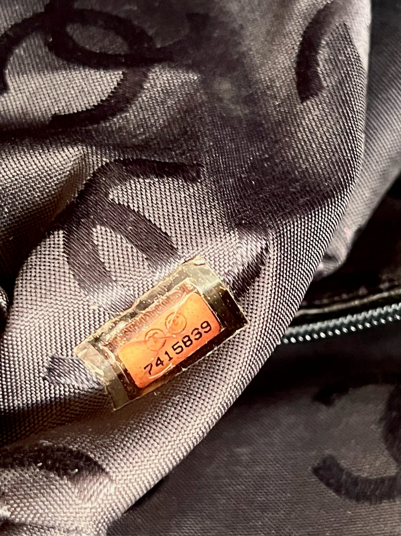 May include: Close-up of a black fabric bag with a brown leather tag that reads "7415839".