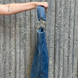 May include: A blue denim tote bag with a silver chain strap. The bag has a faded look and is made of a durable material.