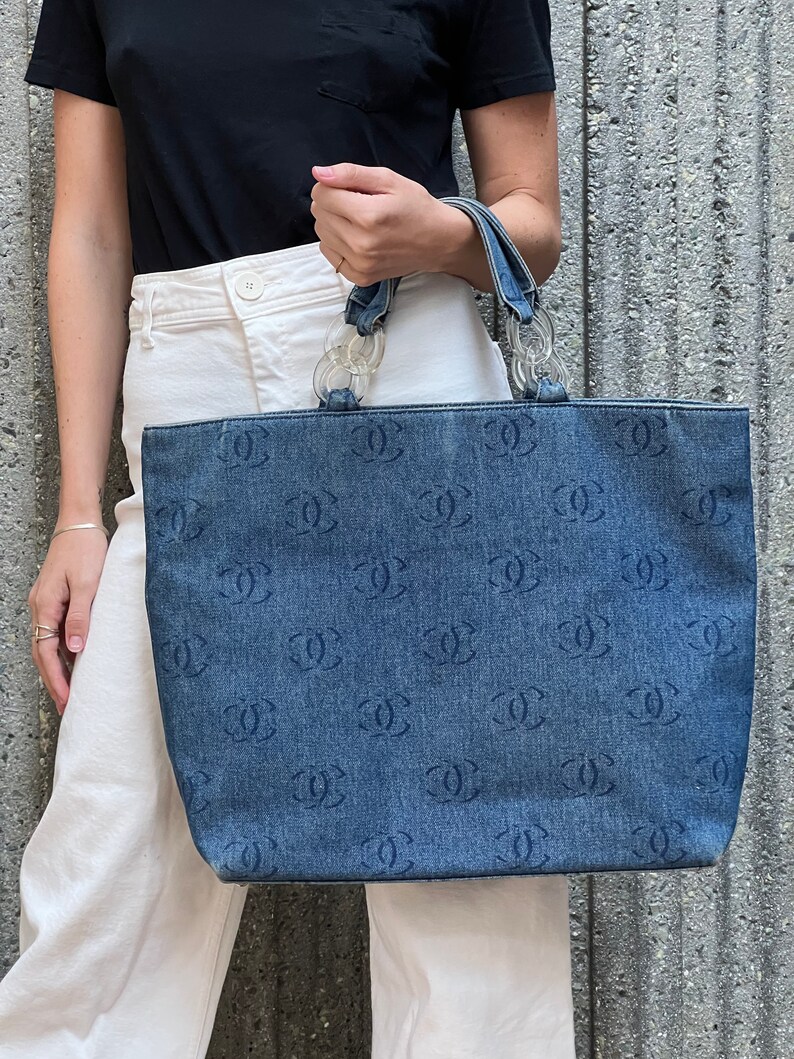 May include: A blue denim tote bag with a clear plastic handle and a repeating pattern of the letter "C".