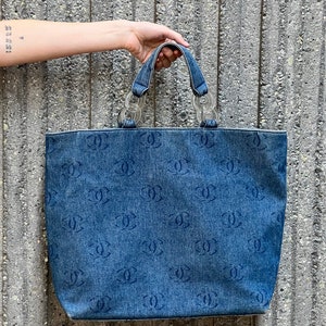 May include: A blue denim tote bag with a repeating logo pattern and silver chain handles.