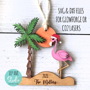 May include: A wooden Christmas ornament featuring a pink flamingo wearing a Santa hat, a palm tree, and a sun. The ornament is personalized with the text "2021 The Millers". The ornament is designed for use with Glowforge or CO2 lasers.