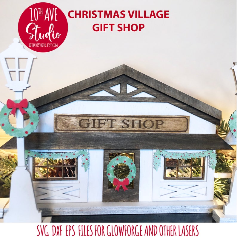 May include: A white wooden Christmas village gift shop with a brown roof and a sign that reads "Gift Shop". The shop has two windows with wreaths and garlands. The shop is lit up with string lights. SVG DXF EPS files for Glowforge and other lasers.