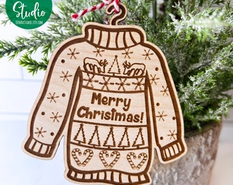 Könnte beinhalten: Ein Weihnachtsbaumschmuck aus Holz in Form eines hässlichen Pullovers mit dem Text "Frohe Weihnachten!" in der Mitte. Der Schmuck ist mit Schneeflocken, Zuckerstangen und Weihnachtsbäumen verziert.