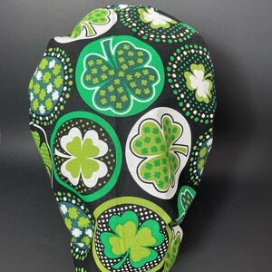 May include: A black scrub hat with a green and white shamrock pattern. The shamrocks are in circles with white polka dots.