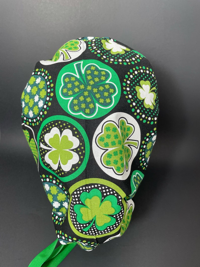 May include: A black scrub hat with a green and white shamrock pattern. The shamrocks are in circles with white polka dots.