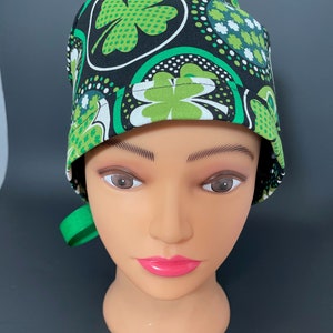 May include: A black and green scrub hat with a four-leaf clover pattern. The hat has a green tie.