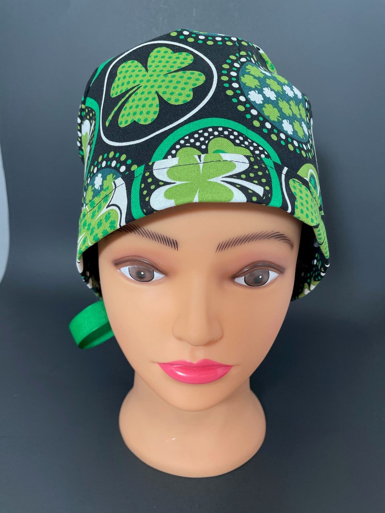 May include: A black and green scrub hat with a four-leaf clover pattern. The hat has a green tie.