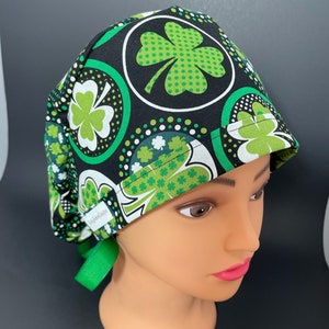 May include: A black scrub hat with a green shamrock pattern. The hat has a green tie and the text "Scrubs & Co." is visible on the side.