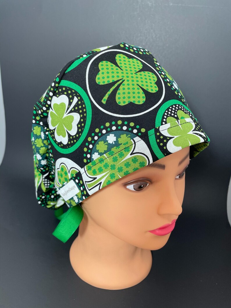 May include: A black scrub hat with a green shamrock pattern. The hat has a green tie and the text "Scrubs & Co." is visible on the side.