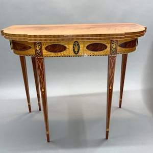 May include: A wooden table with a curved top and intricate inlaid designs. The table has four legs with decorative details and a dark wood finish.